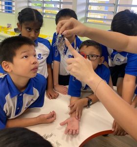Science teacher showing students how a magnet attracts metals such as paper clips.